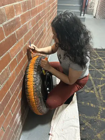 Nelliza rolling a painted tyre across fabric against a wall